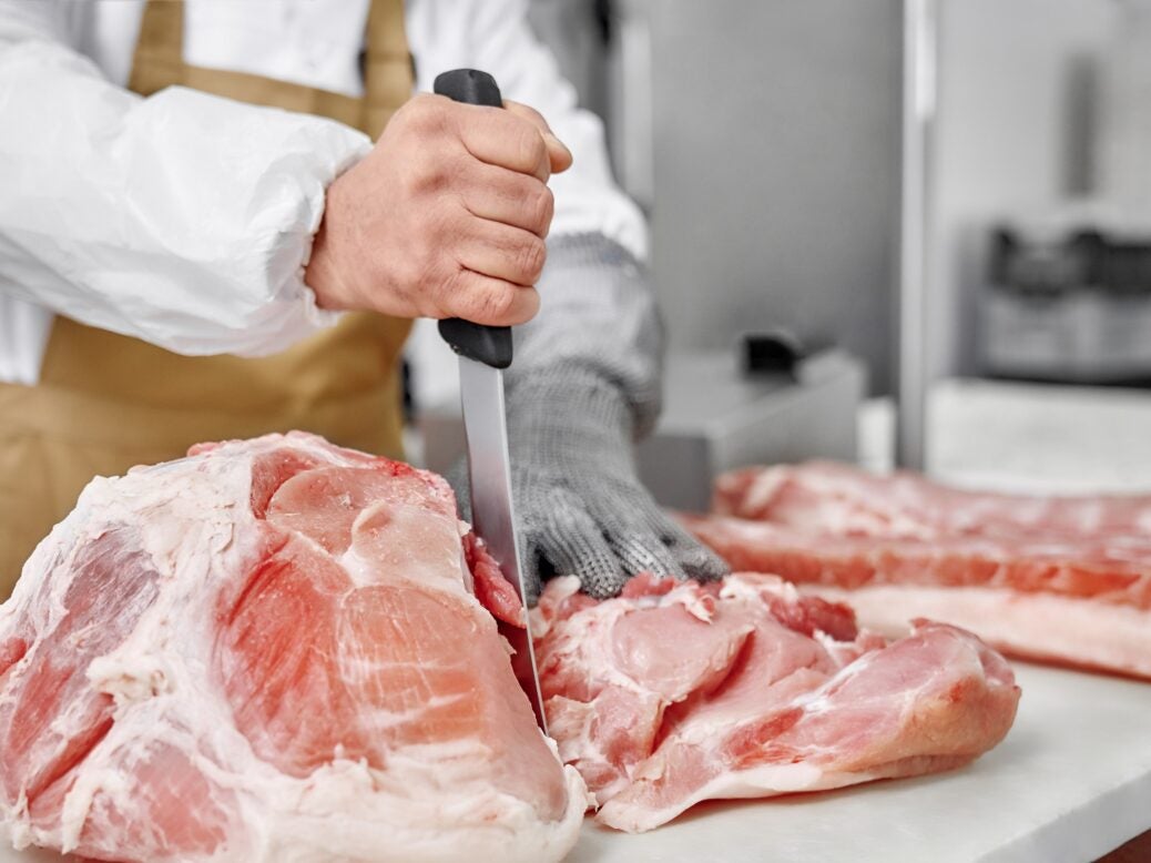 Butcher in gloves cutting fresh meat with knife