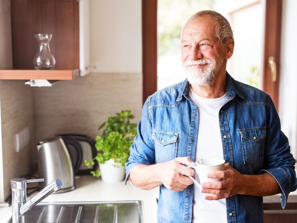 Happy senior man holding a cup of coffee in the kitchen.