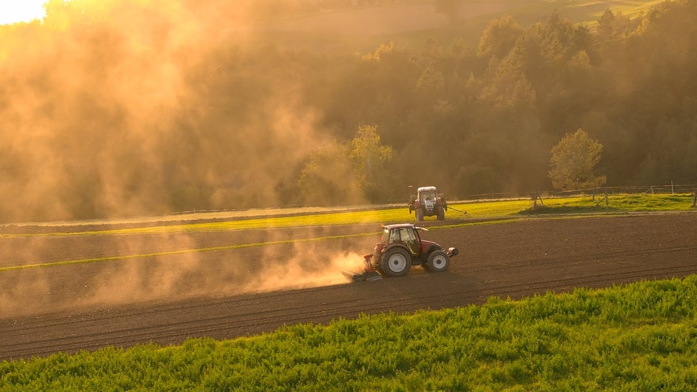  Farmers prepare the field for winter rest and planting in spring season. Two tractors ploughing agricultural land on a sunny hillside, with late afternoon sun casting a warm glow